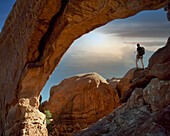 USA, Utah, Arches National Park, Kletterer unter Felsbogen bei Sonnenuntergang
