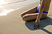 Frau im Bikini am Strand sitzend, tiefer Ausschnitt