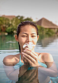 Thailand, Koh Samui Island, Portrait of smiling woman holding frangipani flower in water