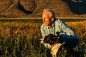 USA, Idaho, Bellevue, Senior man with border collie in field at sunset