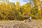 USA, Idaho, Hailey, Rückansicht einer älteren Frau, die sich im Herbst auf einer Bank am Fluss entspannt