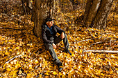 Älterer Mann sitzt an einem Baum im Herbstwald