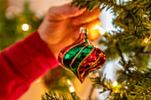 Hand hängt Glasweihnachtsschmuck an den Weihnachtsbaum