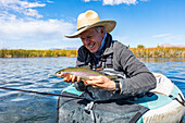 Senior fly fisherman holds rainbow trout before releasing back into spring creek