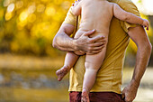 Father holding naked son (2-3) outdoors