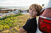 Porträt eines Jungen (8-9), der sich an einen Geländewagen lehnt