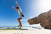South Africa, Western Cape, Boy (8-9) jumping off rock at beach in Lekkerwater Nature Reserve