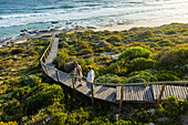 Südafrika, Westkap, Mutter und Tochter (16-17) spazieren auf Holzbrücke am Meer im Lekkerwater Naturreservat