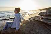 South Africa, Western Cape, Girl (16-17) sitting on beach at sunset in Lekkerwater Nature Reserve