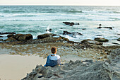 Südafrika, Westkap, Mädchen (16-17) sitzt am Strand und schaut auf das Meer im Lekkerwater Nature Reserve