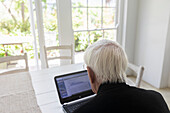 Älterer Mann arbeitet zu Hause an einem Laptop