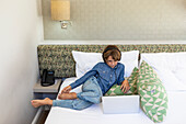 Boy (8-9) in hotel room looking at laptop