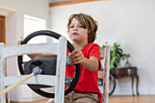 Junge (8-9) spielt mit dem Lenkrad im Wohnzimmer