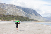 Südafrika, Hermanus, Junge (8-9) trägt Bodyboard am Strand