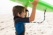 Junge (8-9) trägt Bodyboard am Strand