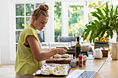 Girl (16-17) using laptop while preparing meal in kitchen