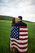 Junges, in die amerikanische Flagge gehülltes Paar küsst sich in einem Weizenfeld
