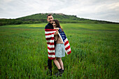 Lächelndes junges Paar mit amerikanischer Flagge in einem Weizenfeld