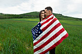 Young couple wrapped in American flag in wheat field