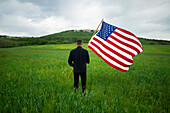 Rückansicht eines Mannes mit amerikanischer Flagge in einem Weizenfeld