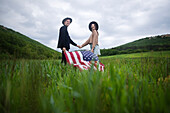 Junges Paar mit amerikanischer Flagge, das sich im Weizenfeld an den Händen hält