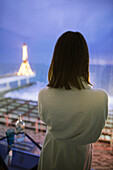 Rückansicht einer Frau im Bademantel in einem Hotel mit Blick auf das nächtliche Meer
