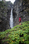 Russland, Karatschai-Tscherkessien, Arkhyz, Kaukasusgebirge, Wanderer steht in der Nähe eines Wasserfalls
