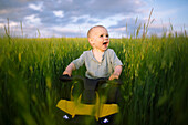 Baby boy (12-17 months) on toy vehicle in agricultural field