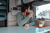 Mann sitzt in einem Wohnmobil und trinkt Tee