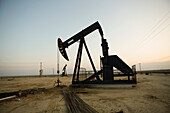 Silhouette eines Pumpenhebers auf einem Ölfeld bei Sonnenuntergang
