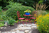 Roter Tisch und Stühle mit blauem Topf im Blumengarten. Marion Grafschaft, Illinois (PR)