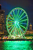 USA, Bundesstaat Washington, Seattle. Die Skyline der Innenstadt in der Abenddämmerung, von der Elliott Bay aus gesehen in Richtung Osten, mit dem Seattle Great Wheel.