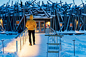 Person, die in der Abenddämmerung auf dem gefrorenen Steg steht, der das schwimmende Arctic Bath Hotel mit dem Ufer verbindet, Harads, Lappland, Schweden, Skandinavien, Europa