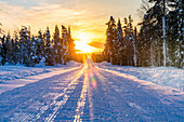 Sonnenuntergang über einer leeren, verschneiten Straße, Lappland, Finnland, Europa