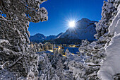 Moon glowing over the snowy bell tower of Chiesa Bianca and woods in winter, Maloja, Bregaglia, Engadine, Canton of Graubunden, Switzerland, Europe