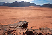 Eine Person steht auf einem Felsen über der weiten Ebene der Wadi-Rum-Wüste, UNESCO-Welterbe, Jordanien, Naher Osten