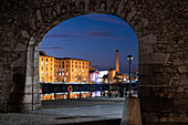 Das Albert Dock und das Pumphouse bei Nacht durch einen Rest der ursprünglichen Hafenmauer betrachtet, Liverpool Waterfront, Liverpool, Merseyside, England, Vereinigtes Königreich, Europa