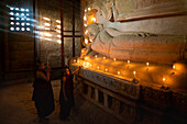 Zwei Mönchsnovizen zünden eine Kerze neben einer buddhistischen Statue im Tempel an, Bagan (Pagan), UNESCO-Weltkulturerbe, Myanmar (Burma), Asien