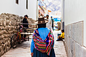 Frau geht in enger Straße mit traditioneller bunter peruanischer Tasche auf dem Rücken, Pisaq, Peru, Südamerika