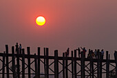 Spaziergänger auf der U-Bein-Brücke über den Taung Tha Man-See bei Sonnenuntergang, Amarapura, Mandalay, Myanmar (Birma), Asien