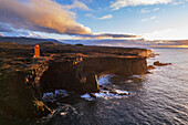 Luftaufnahme des orangefarbenen Svortuloft-Leuchtturms auf den Basaltklippen bei Sonnenuntergang, Snaefellsbaer, Snaefellsjokull-Nationalpark, Snaefellsens-Halbinsel, Vesturland, Westisland, Island, Polargebiete