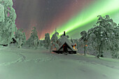 Winter frame of a hut lit by the green Northern Lights (Aurora Borealis) in the icy wood with trees covered with snow, Pallas-Yllastunturi National Park, Muonio, Lapland, Finland, Europe