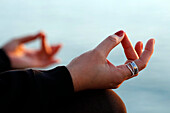 Woman practising yoga meditation by the sea at sunset as concept for silence and relaxation, close-up on hand, gyan mudra, Spain, Europe