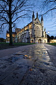 Winchester Cathedral floodlit at night in winter with reflections on wet pavement in foreground, Winchester, Hampshire, England, United Kingdom, Europe