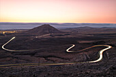 eine Langzeitbelichtung, um die Autospuren während eines sommerlichen Sonnenuntergangs entlang der Straße in der Nähe des Tindaya-Berges einzufangen, Fuerteventura, Kanarische Insel, Spanien, Europa