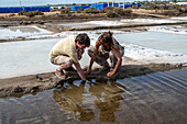 Man and woman reach into salt marshes, Isla Cristina, Spain