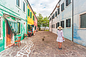 Eine Frau inmitten von Reihen bunter Gebäude in Burano, Venedig, Venetien, Italien, Europa