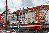 Red and white ship at anchor in a Copenhagen canal. In the background, the characteristic brightly colored Danish houses. Copenhagen, Denmark, Europe