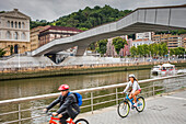 Biking, in Ría del Nervión, in background Pedro Arrupe Bridge and at left Deusto University , Bilbao, Basque Country, Spain