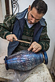 Craftsman at work, decorating a vessel with silver filigree, metalworks souk, medina, Meknes. Morocco